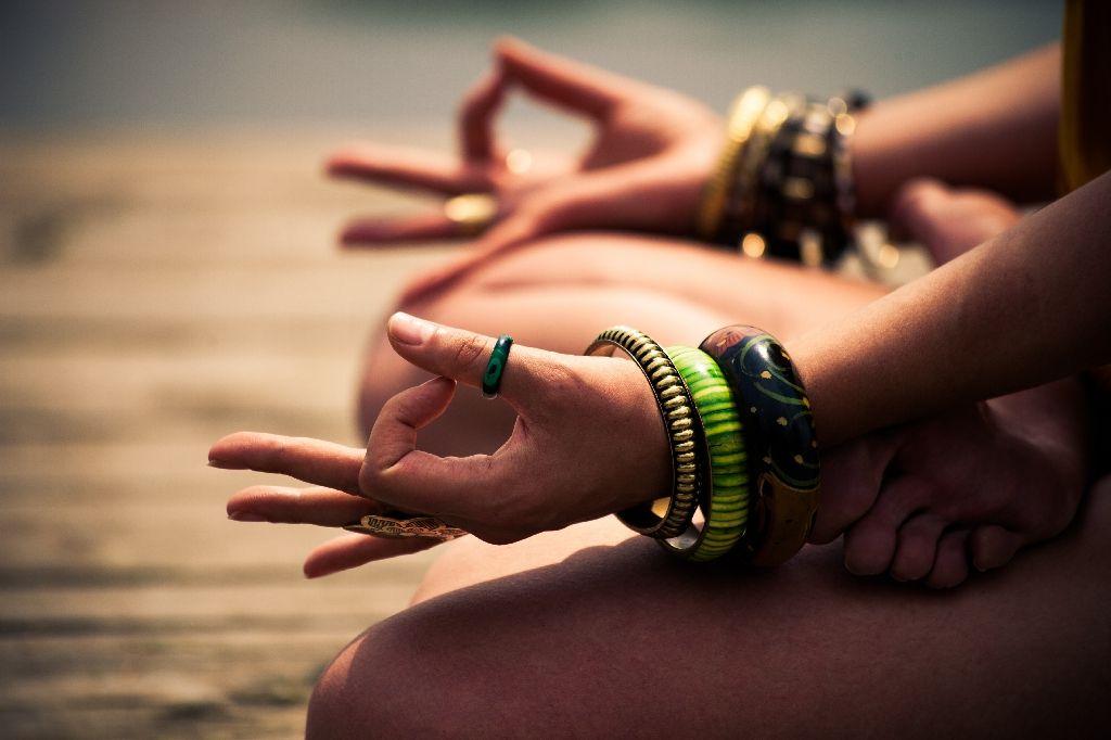 woman in a meditative yoga position lower body outdoor woman in a meditative yoga position sit on wooden pontoon on the lake wearing lot of bracelets and rings lower body
