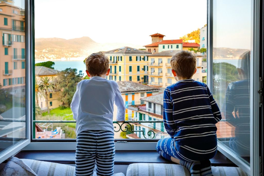 Two little kids boys enjoying view from window on Liguria region in Italy. Awesome villages of Cinque Terre and Portofino. Family vacations in beautiful Italian city with colorful houses