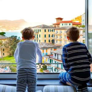 Two little kids boys enjoying view from window on Liguria region in Italy. Awesome villages of Cinque Terre and Portofino. Family vacations in beautiful Italian city with colorful houses
